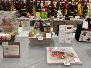 gift baskets and painted photo of a fire truck lined up in from of fire gear hanging in the background